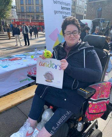 Eine Besucherin im Rollstuhl hält das Kinderbuch "anders" vor sich