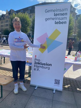 Viola im Vereins-T-Shirt neben unserem Aufsteller mit der Aufschrift Gemeinsam lernen gemeinsam leben