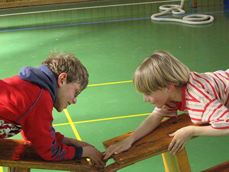 zwei Grundschulkinder auf Rollbrettern in der Turnhalle